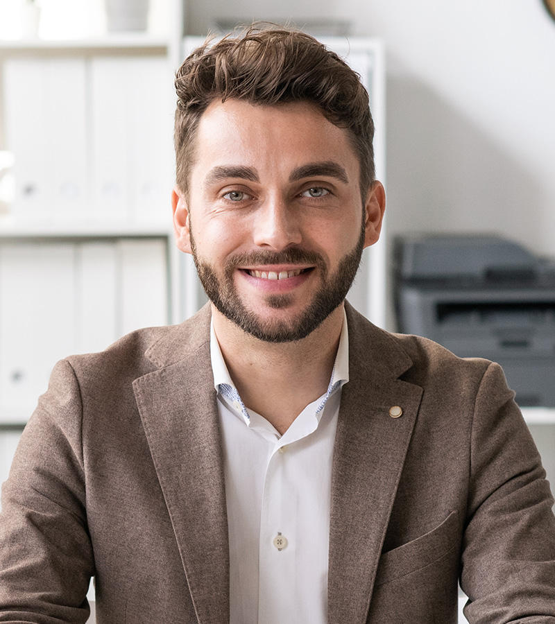 happy young lawyer in formalwear sitting by desk i T7MFNTV